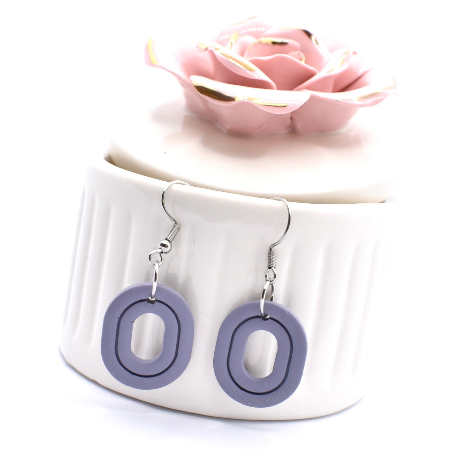 Blue oval shaped clay earrings hanging off the side of a decorative jar 