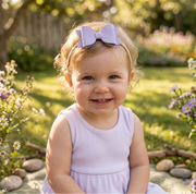 Child wearing a purple dress and purple bow headband with a garden background