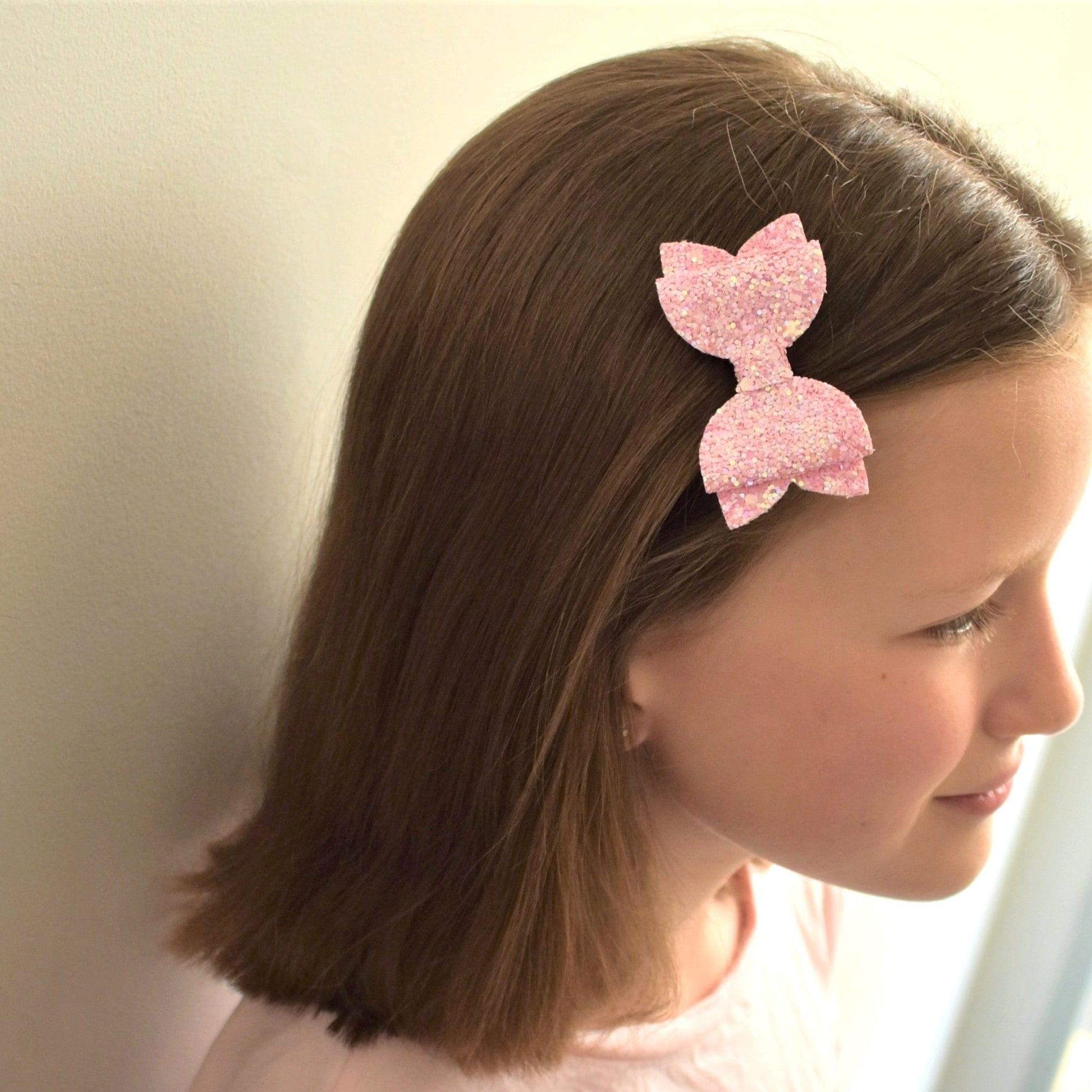 Young girl with a pink glittery bow in her hair against a neutral background